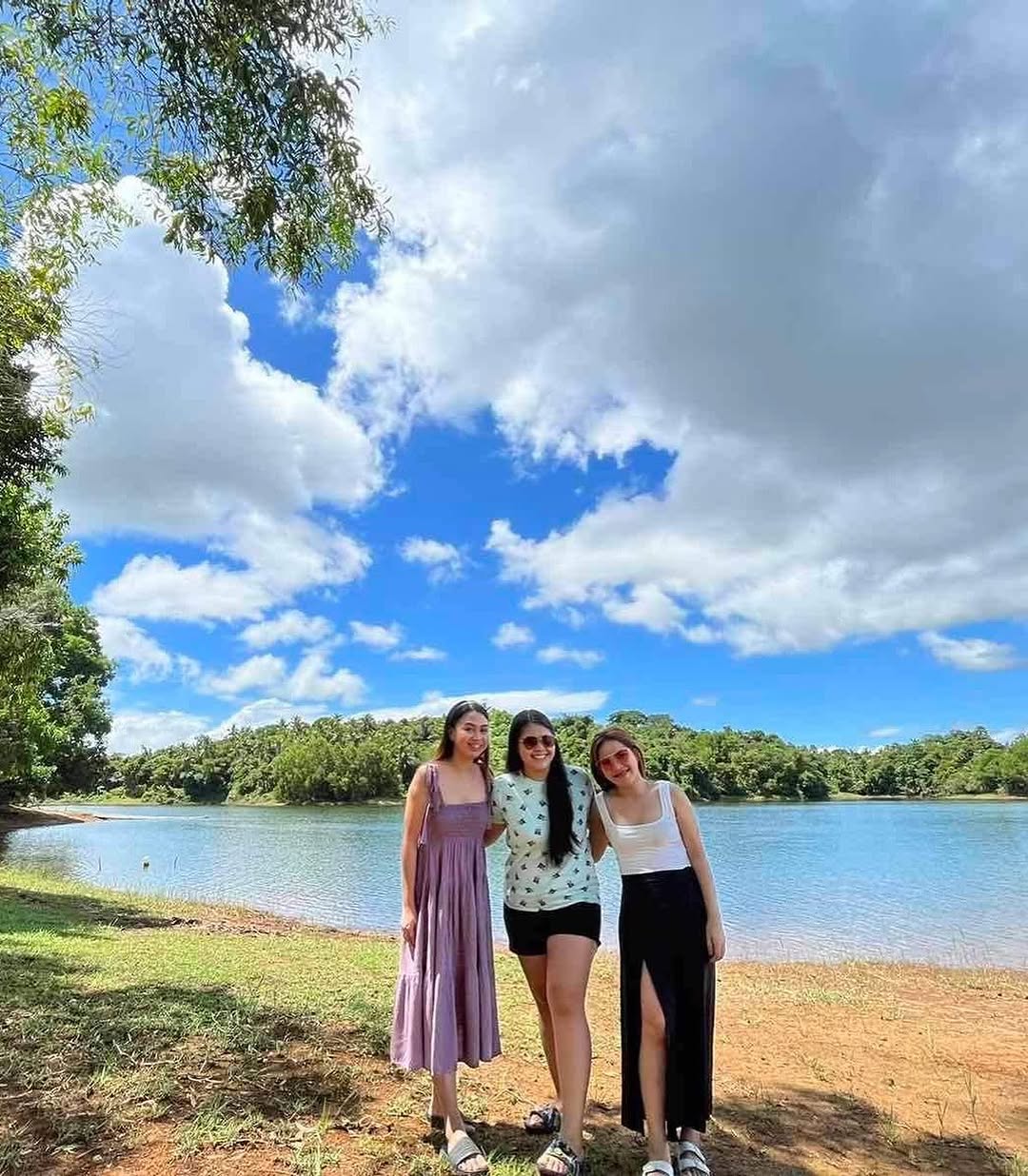 Three guests smiling by the lake shore with forest and blue sky backdrop