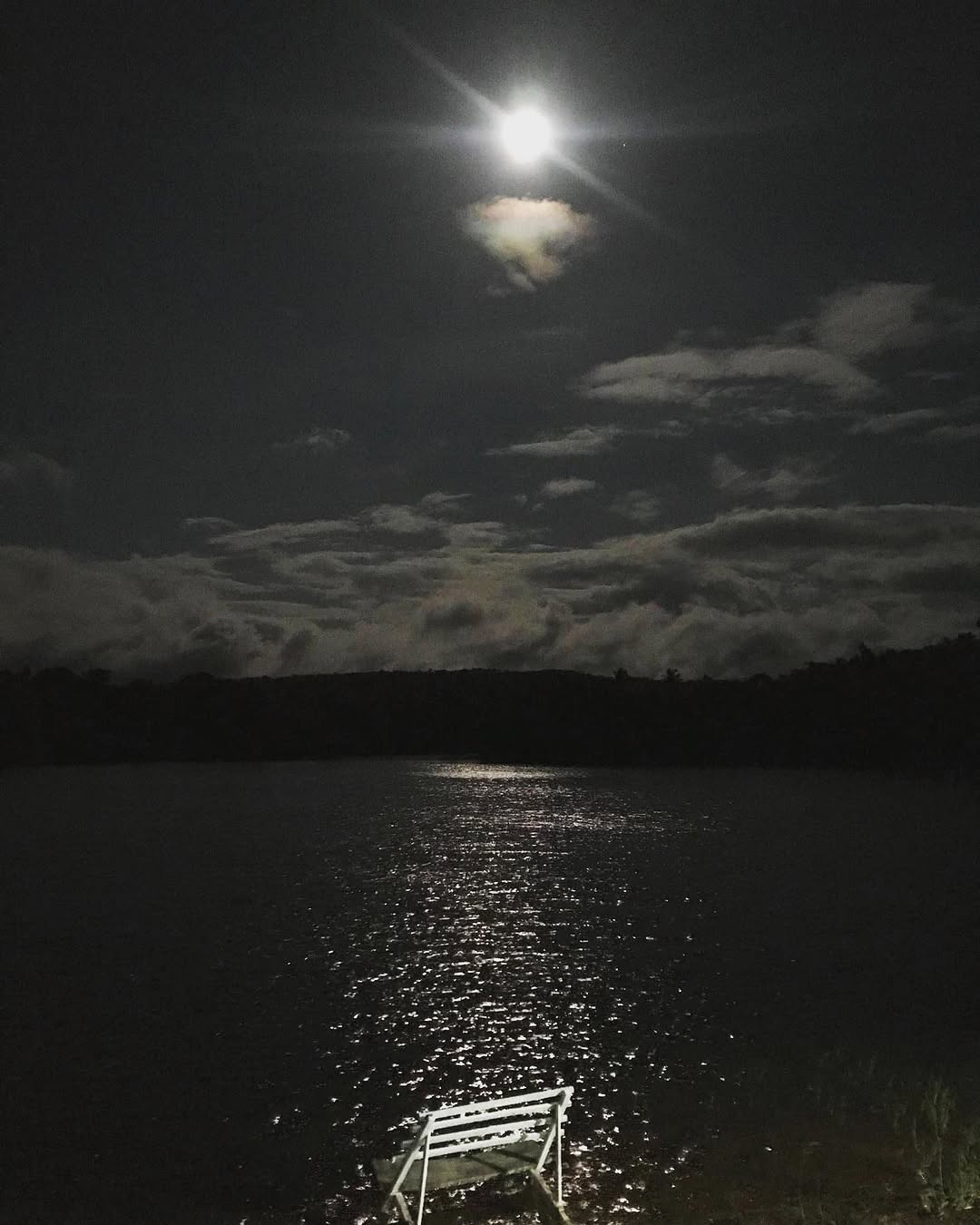 Bright moon over dark Lake Lumot with moonlight shining on the water and a white bench dock