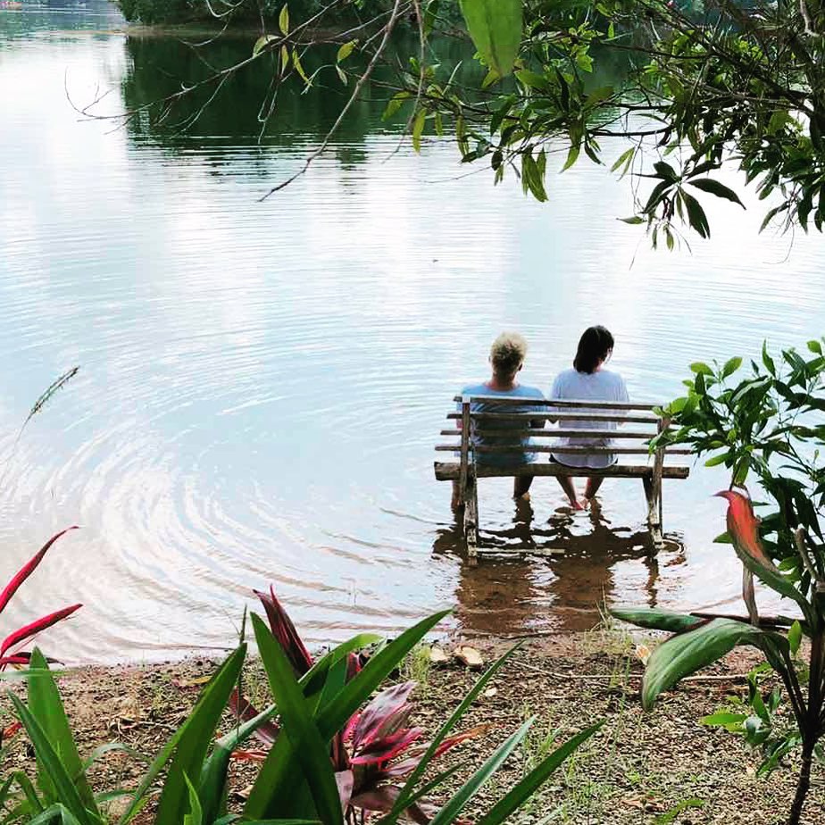 Two guests sitting on a bench in the lake, surrounded by lush greenery