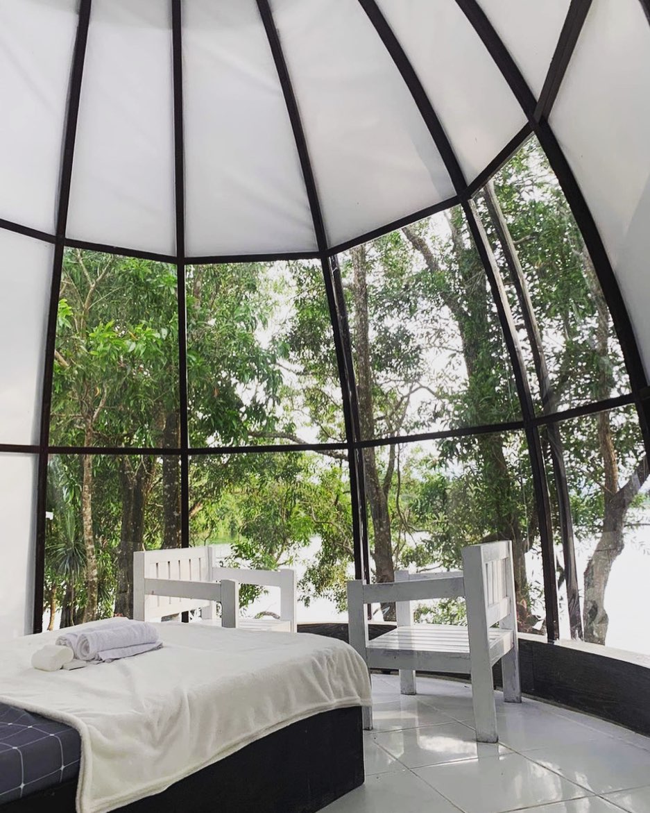 Dome interior — bed and chairs with panoramic lake view through full dome panels