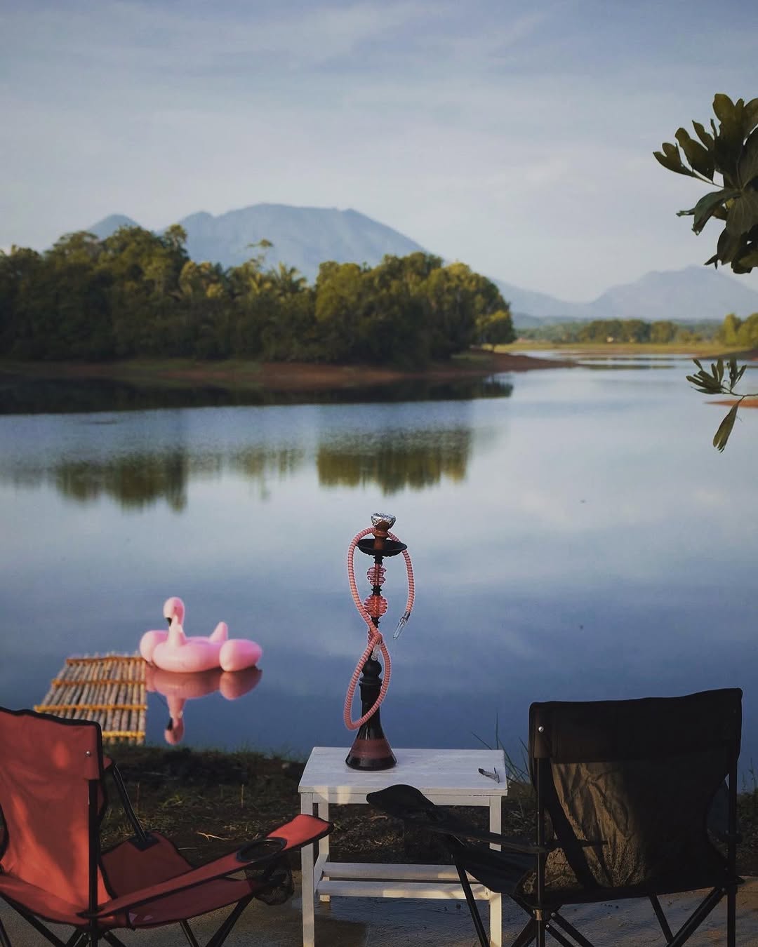 Calm lake with mountain backdrop, flamingo pool floater on the water and camp chairs